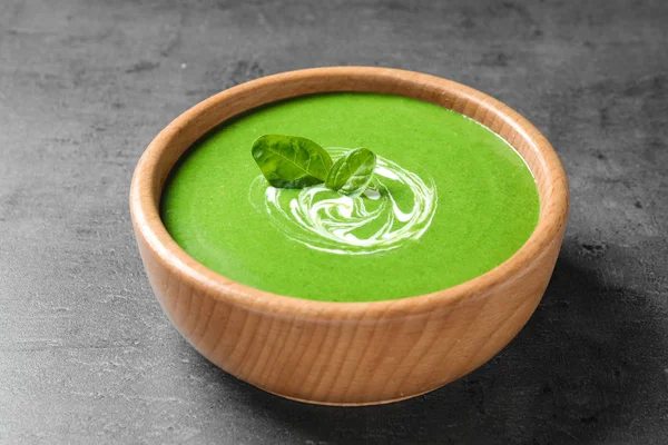Bowl of healthy green soup with fresh spinach on grey table