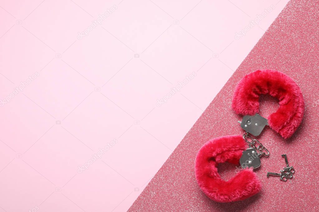 Red fluffy handcuffs and keys on pink background, top view with space for text. Sexual role play accessory