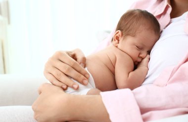 Küçük bebeği evde koltukta oturan genç anne. Metin için alan