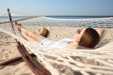 Genç bir kadın plajda hamakta dinleniyor.