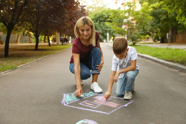 Nanny met schattige kleine jongen tekening huis met krijt op asfalt — Stockfoto