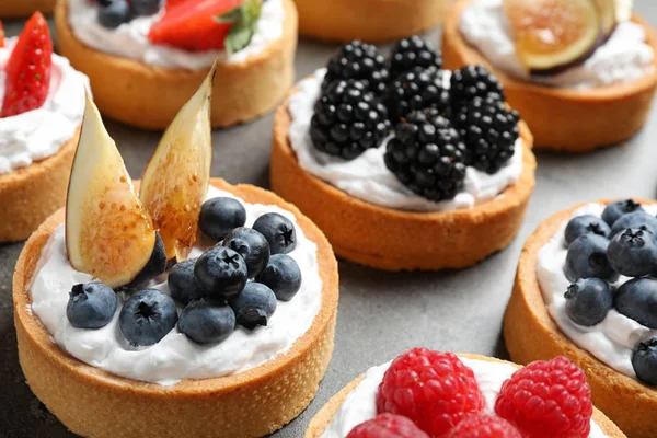 Many different berry tarts on table, closeup. Delicious pastries