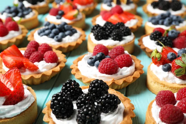 Many different berry tarts on blue wooden table. Delicious pastries — Stock Photo, Image