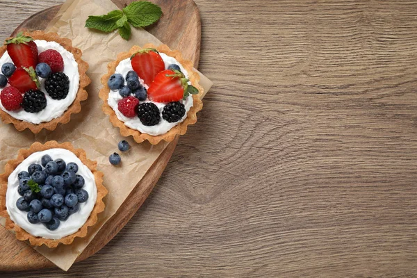 Different berry tarts on wooden table, flat lay with space for text. Delicious pastries