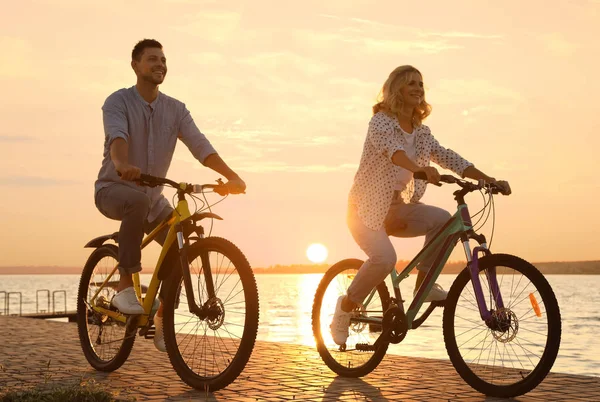 Szép pár lovaglás kerékpárok töltésen naplementekor — Stock Fotó