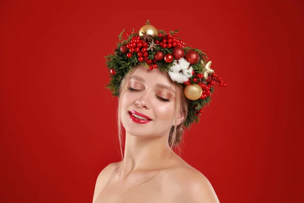 Όμορφη νεαρή γυναίκα φορώντας στεφάνι Χριστουγέννων σε κόκκινο φόντο — Φωτογραφία Αρχείου