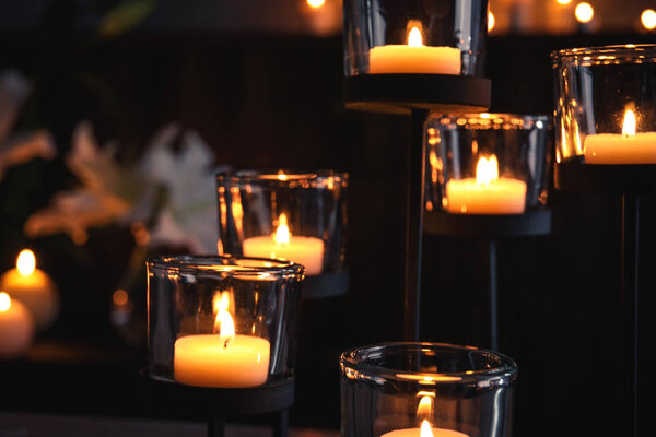 Holder with burning candles in darkness, closeup view. Funeral symbol