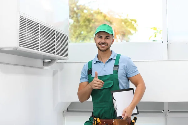 Técnico profissional com prancheta perto de ar condicionado moderno dentro de casa — Fotografia de Stock