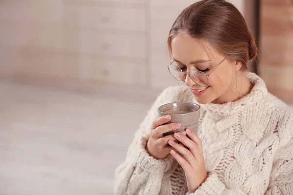 Bella giovane donna con tazza di bevanda calda a casa, spazio per il testo. Atmosfera invernale — Foto Stock