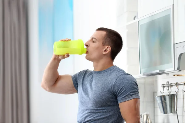 Atletický mladý muž popíjí proteinový koktejl v kuchyni — Stock fotografie