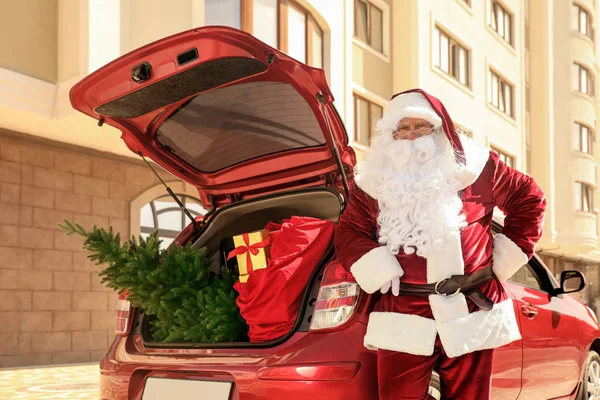 Autentico Babbo Natale vicino auto con abete e borsa piena di regali di Natale in tronco aperto all'aperto — Foto Stock