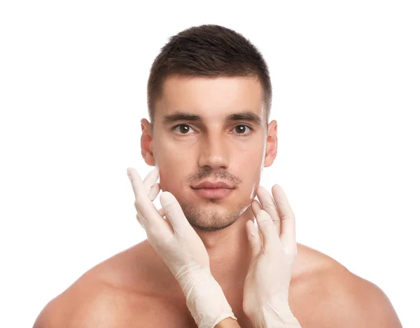 Médico examinando o rosto do homem para cirurgia estética em fundo branco — Fotografia de Stock
