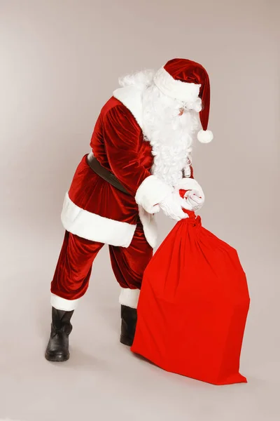 Authentische Weihnachtsmann mit Tasche voller Geschenke auf grauem Hintergrund — Stockfoto