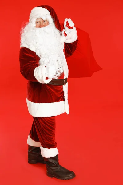 Authentic Santa Claus with bag full of gifts on red background — Stock Photo, Image