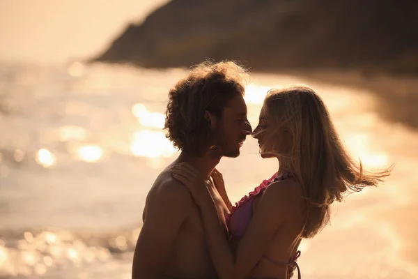年轻女子在比基尼亲吻她的男朋友在海滩上日落。可爱的夫妇 — 图库照片