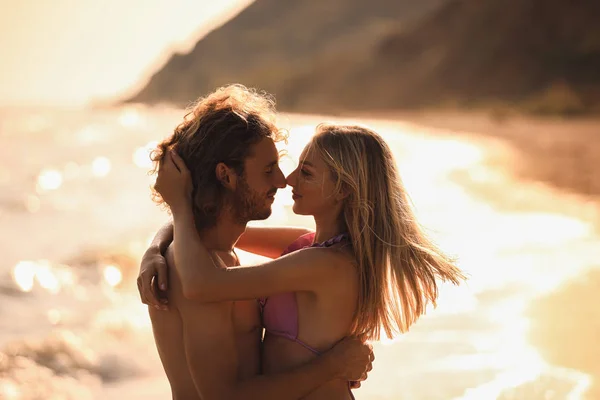 Mujer joven en bikini besando a su novio en la playa al atardecer. Hermosa pareja. —  Fotos de Stock