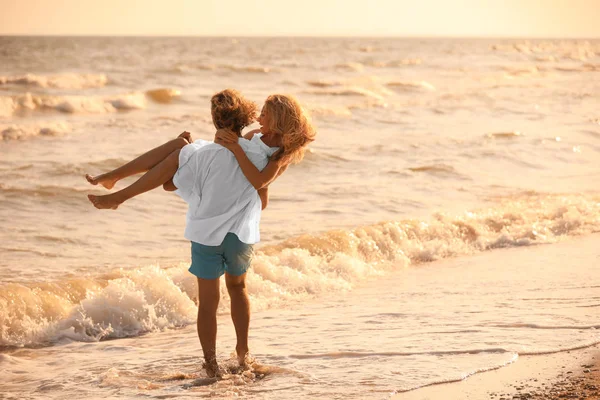 Jovem casal se divertindo na praia ao pôr do sol — Fotografia de Stock