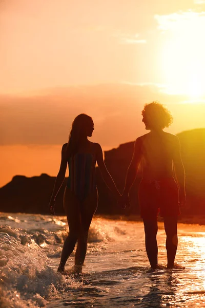 Jeune femme en bikini et son petit ami sur la plage au coucher du soleil. Charmant couple — Photo