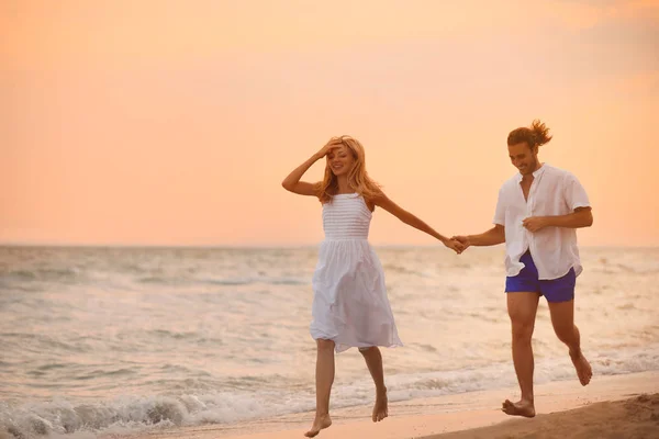 Jovem casal se divertindo na praia ao pôr do sol — Fotografia de Stock