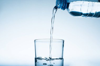 Gri arka plana karşı şişeden cama su dökmek. Ferahlatıcı içecek