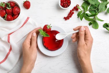Kadın beyaz ahşap masada lezzetli taze kırmızı jöle yeme, üst görünümü