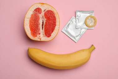 Muz ve pembe arka plan üzerinde kesilmiş greyfurt ile Prezervatif, düz yatıyordu. Güvenli seks