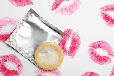 Beyaz arka planda prezervatif ve ruj öpücük izleri, üst görünüm. Güvenli seks