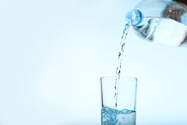 Nalewanie wody z butelki do szklanki na niebieskim tle. Orzeźwiający napój — Zdjęcie stockowe