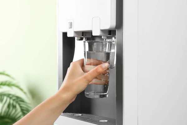 Mujer llenando vidrio de enfriador de agua en el interior, primer plano. Bebida refrescante —  Fotos de Stock