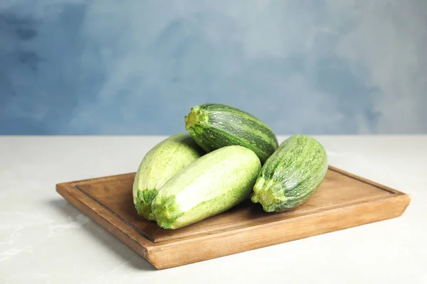 Fresh ripe green zucchinis on light table against blue background, space for text