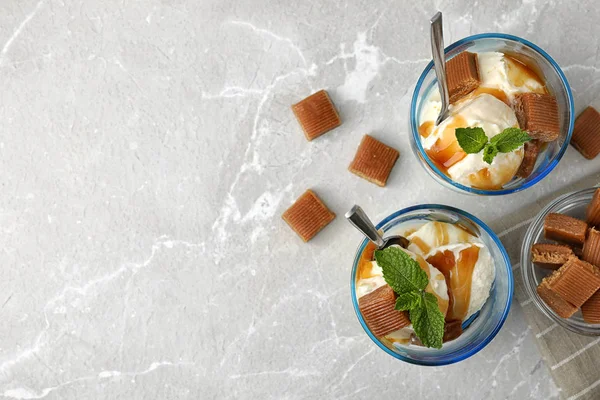 Стаканы вкусного мороженого с карамельным соусом, конфеты и мята на светло-сером мраморном столе, плоский уголок. Пространство для текста — стоковое фото