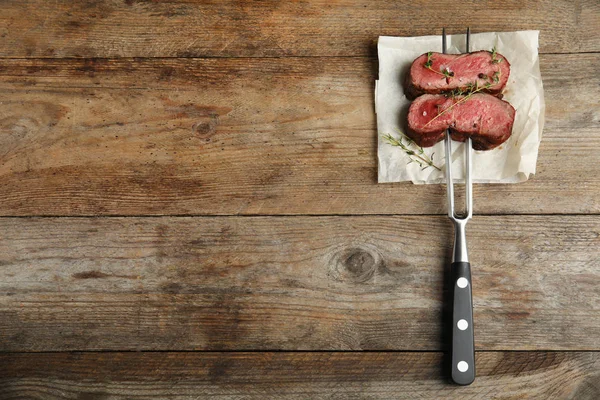 Tenedor con rodajas de carne sobre mesa de madera, vista superior. Espacio para texto — Foto de Stock