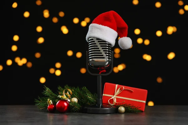 Micrófono con sombrero de Santa Claus y decoraciones en mesa de piedra gris contra luces borrosas. Música navideña — Foto de Stock
