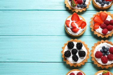 Mavi ahşap masa üzerinde birçok farklı berry tarts, düz metin için yer ile yatıyordu. Lezzetli hamur işleri