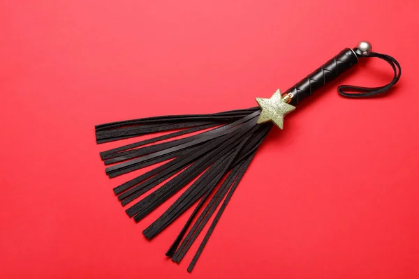Black whip for sexual role play and gold star on red background, top view — Stock Photo, Image