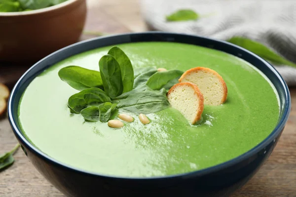 Bowl of healthy green soup with fresh spinach on wooden table, closeup view
