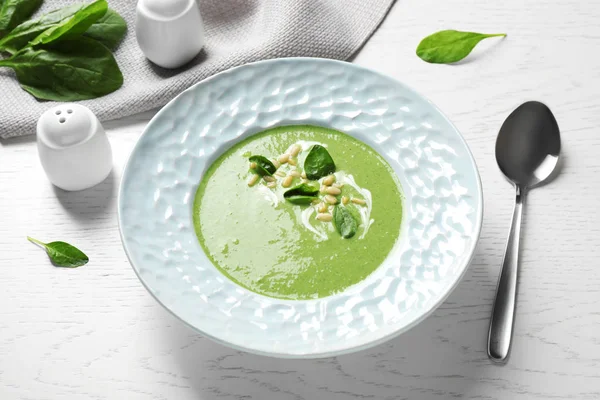 Plate of healthy green soup with fresh spinach on white wooden table