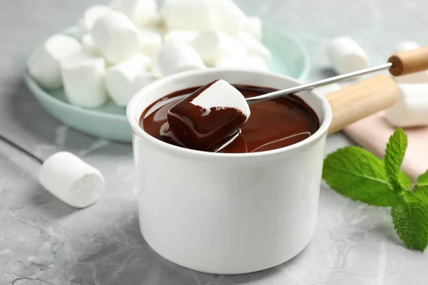 Marshmallow in Fonduetopf mit dunkler Schokolade auf Marmortisch tauchen, Nahaufnahme — Stockfoto