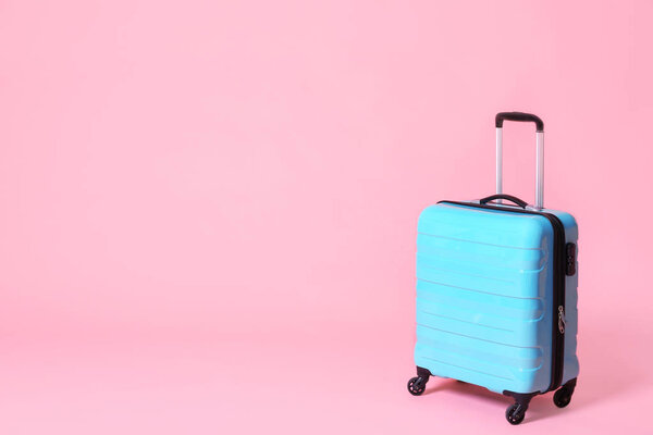 Modern blue suitcase on light pink background. Space for text