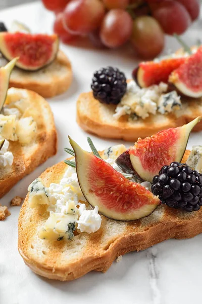 Bruschettas with cheese, figs and blackberries served on white table, closeup