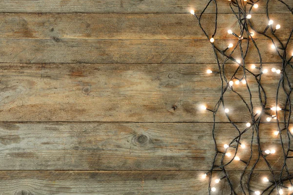 Leuchtende Weihnachtsbeleuchtung auf hölzernem Hintergrund, Draufsicht. Raum für Text — Stockfoto