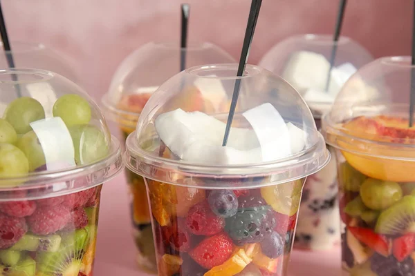 Ensalada de frutas frescas y sabrosas en tazas de plástico sobre fondo rosa, primer plano — Foto de Stock