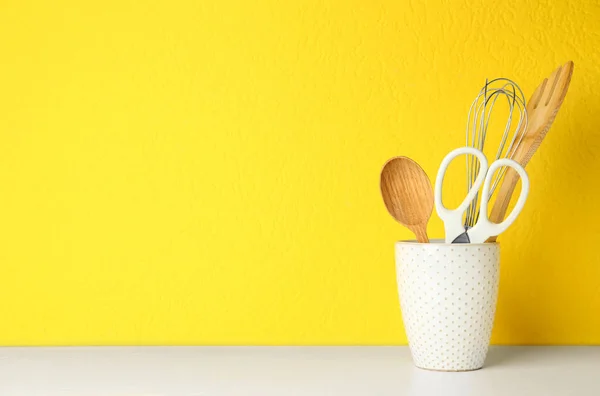 Houder met keukengerei op witte tafel tegen gele achtergrond. Ruimte voor tekst — Stockfoto