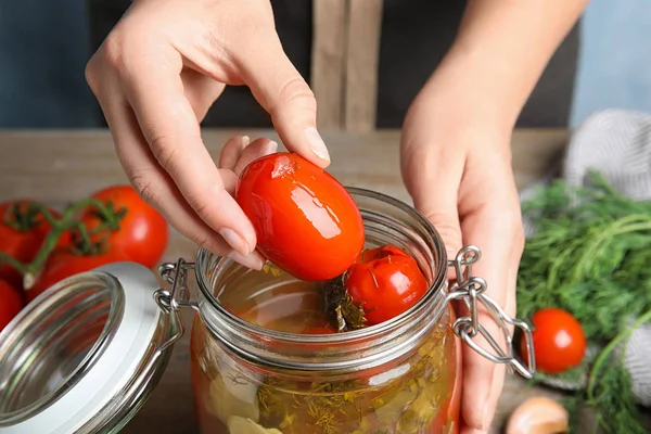 Vrouw nemen gepekelde tomaat van glazen pot bij tafel, close-up bekijken — Stockfoto
