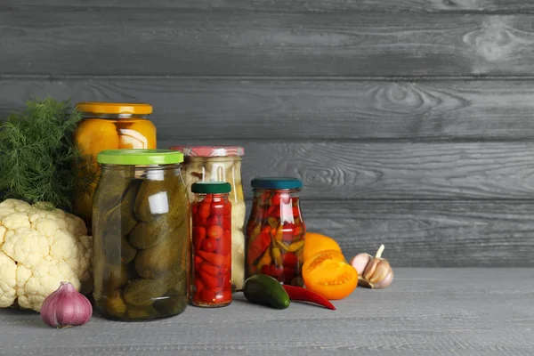 Glass jars with pickled vegetables on wooden table against grey background. Space for text