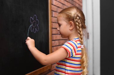 Cute little left-handed girl drawing on chalkboard near brick wall clipart