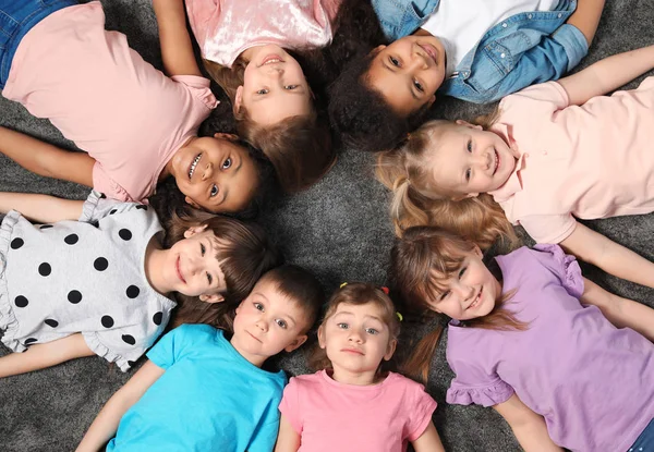Очаровательные маленькие дети лежат на полу вместе в помещении, вид сверху. Развлечения в детском саду — стоковое фото