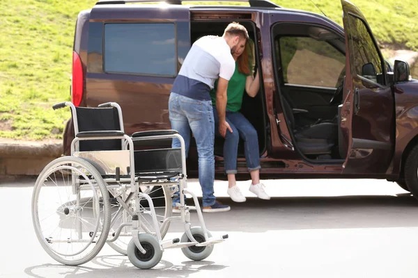 Młody mężczyzna pomaga kobiecie wyjść z Vana, skupić się na wózku inwalidzkim na zewnątrz — Zdjęcie stockowe