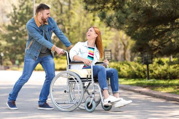 Szczęśliwa kobieta na wózku inwalidzkim i młodym mężczyzną w parku w słoneczny dzień — Zdjęcie stockowe