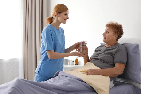 Infermiera che dà un bicchiere d'acqua a una donna anziana in casa. Assistenza medica — Foto Stock